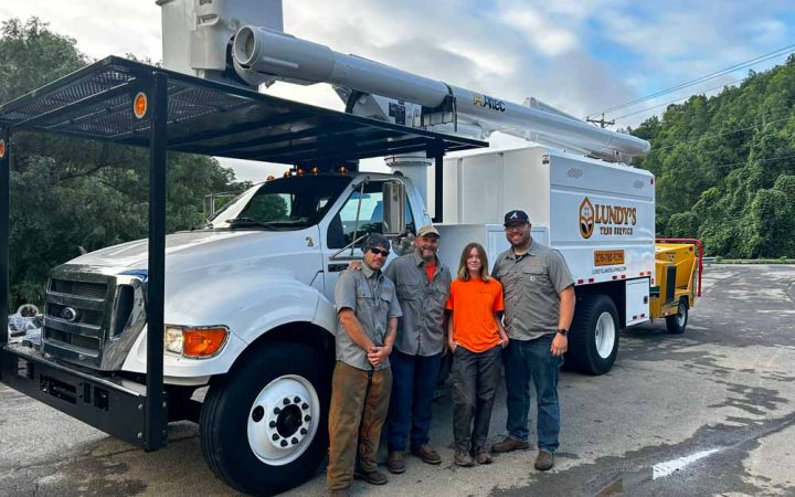 A team photo of tree service professionals in front of their specialized truck and equipment, reflecting teamwork and readiness for tree maintenance tasks.