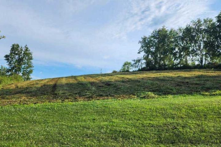 A lush green hill captured after landscaping efforts, showcasing a smooth gradient and well-maintained grass under a vivid blue sky.