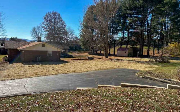 A residential area showing clear grounds after tree removal, with a house in the background.