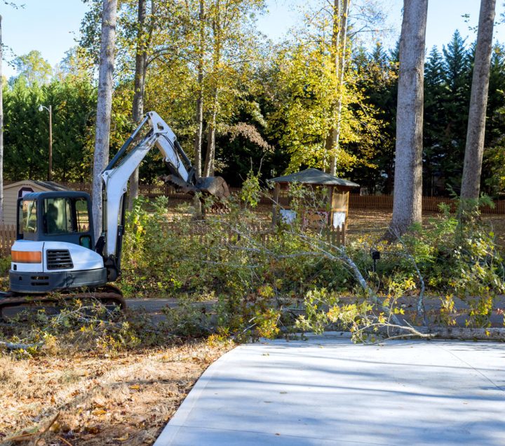 An excavator removing fallen branches near a suburban home, highlighting mechanical tree removal.